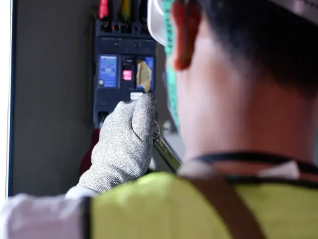 Electrician in a safety vest working on a breaker panel
